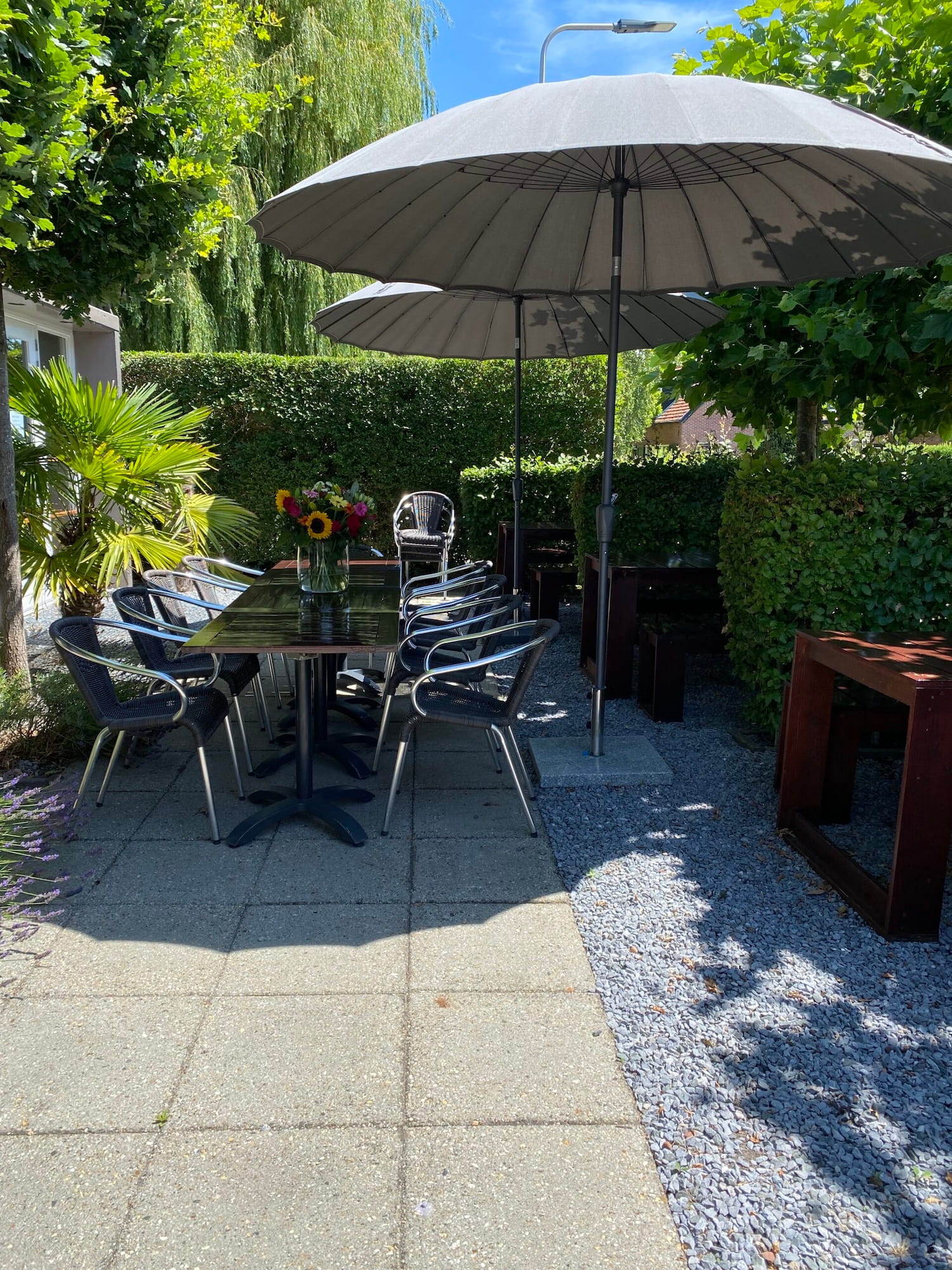 Buiten vergaderen in luie stoelen, onder een parasol en een grote bos bloemen op de tafel, alles strak in de verf